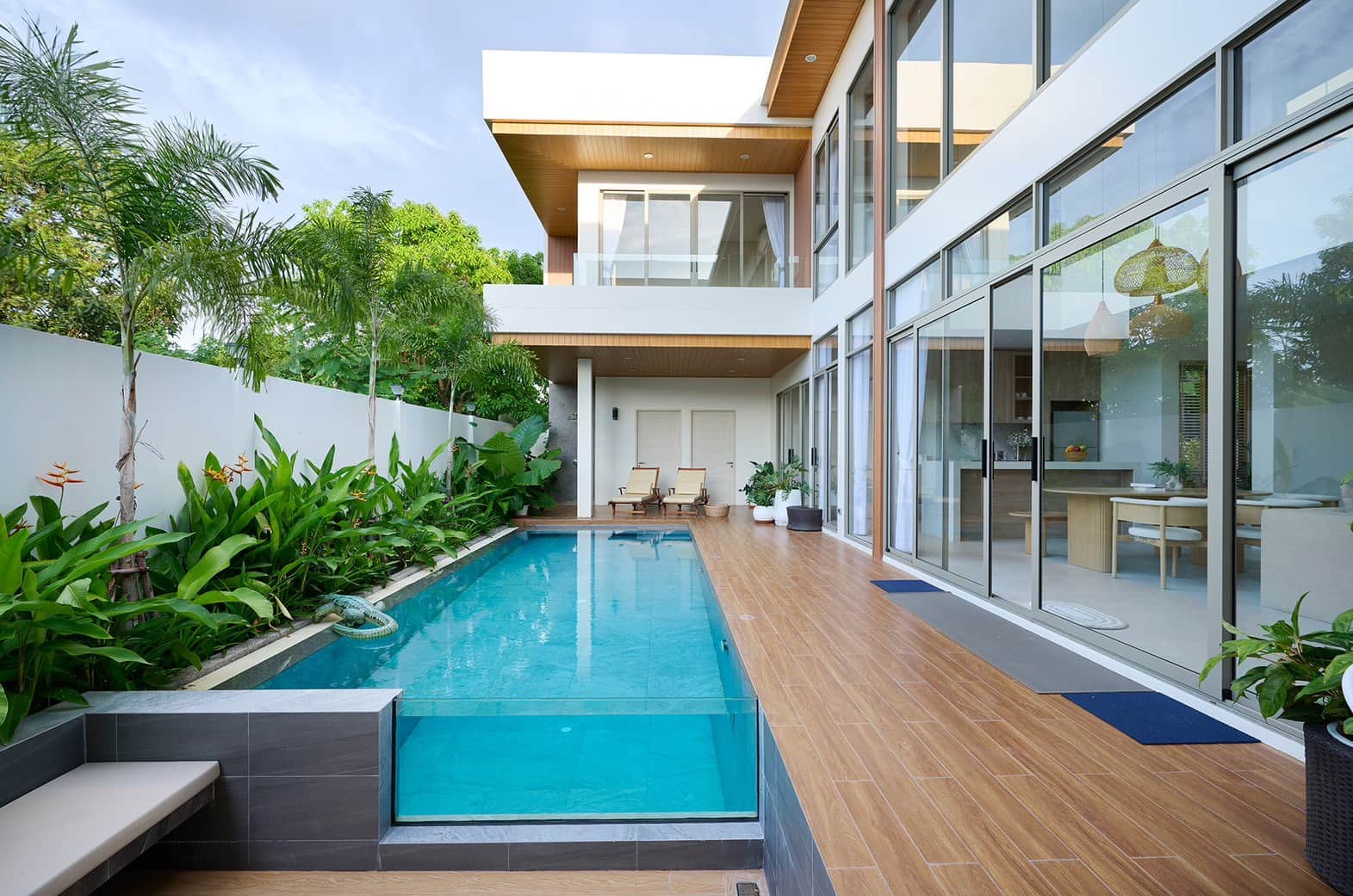 Villa Belcasa at dusk: the private pool with a glass wall, wooden deck and the two-storey villa behind